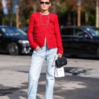 Guest wears black sunglasses, silver layered necklaces, bright red tweed Chanel blazer jacket, washed light blue denim jean pants, shiny black...