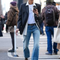 Guest wears black sunglasses, white Calvin Klein Jeans print t-shirt, cream unbuttoned long sleeve shirt, black blazer jacket, black leather belt,...