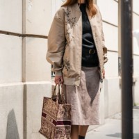 Guest wears black t-shirt, beige printed jacket, beige midi skirt, Dior burgundy tote bag, black loafers, outside Dior Homme, during the Haute...