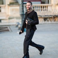 Guest wears black tailored coat, shiny black leather bag, black pants, shiny black leather shoes , outside Louis Vuitton, during the Paris Fashion...