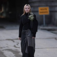 Guest wears black turtleneck sweater, black cropped blazer jacket / short cost, grey denim shoulder bag with white flowers inside, grey denim / jeans...