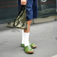 Guest wears blue denim shorts, a green sequined handbag, white socks, green plastic with yellow eyes and red lips mules in shape of frog , outside JW...