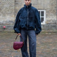 Guest wears blue jacket, Dior saddle bag, wrapped wide leg denim jeans outside TG Botanical during the Copenhagen Fashion Week Autumn/Winter 2025 on...