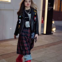 Guest wears blue jeans, a red and black checkered skirt, red boots, and a black leather jacket with knitted colorful elements during the Tashkent...