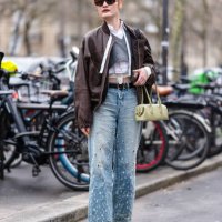 Guest wears bright orange hair, dark brown sunglasses, gold earrings, white buttoned up long sleeve cropped shirt, dark gray v-neck long sleeve...