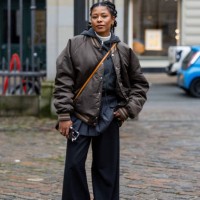 Guest wears brown bomber jacket, grey skirt, pants, black Louis Vuitton bag outside TG Botanical during the Copenhagen Fashion Week Autumn/Winter...