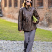Guest wears brown leather jacket, grey pleated skirt outside Herskind during the Copenhagen Fashion Week AW24 on January 31, 2024 in Copenhagen,...