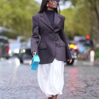 Guest wears brown sunglasses, a black turtleneck pullover, black blazer jacket, a white skirt, a light blue leather Balenciaga bag with crocodile...