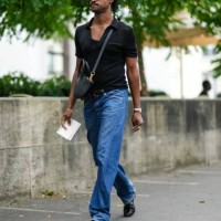 Guest wears brown sunglasses from Celine, a gold necklace, a black short sleeves t-shirt, a black matte leather crossbody bag, blue denim large...