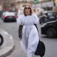 Guest wears brown sweater under white puffy maxi dress, sneakers, tote bag and black sunglasses and white sneaker outside Dries Van Noten show during...