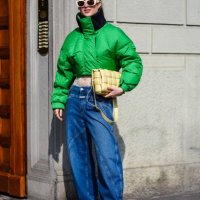 Guest wears cream sunglasses, a green bomber jacket, a light yellow leather quilted bag, blue denim jeans / pants, black leather shoes, outside...