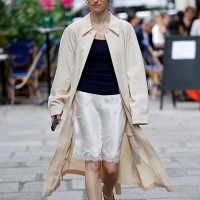 Guest wears dark blue top, white silk skirt with lace, beige trench coat, outside Lemaire, during the Menswear Spring/Summer 2026 show as part of...