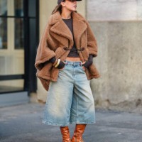 Guest wears dark brown Baseball hat, dark brown long sleeve shirt, light brown teddy bear oversized Max Mara coat, washed denim jean jorts, light...