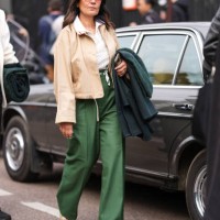 Guest wears dark brown sunglasses, white sheer mesh pattern polo Lacoste shirt, silver necklace, light brown unbuttoned jacket, dark green high...