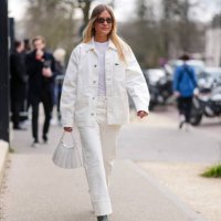 Guest wears dark brown sunglasses, white t-shirt, gold layered necklaces, cream oversized denim jean Lacoste jacket, cream loose denim jean cuffed...