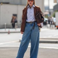 Guest wears dark brown sunglasses with orange lenses, light blue buttoned up long sleeve shirt, dark brown blazer jacket, dark brown leather belt,...