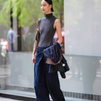 Guest wears dark gray sleeveless turtleneck shirt, dark gray belted bag, navy blue denim jean pants, black jacket in hand, white sneaker shoes,...