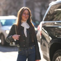 Guest wears dark red sunglasses, white bow long sleeve shirt, shiny black buttoned up cropped leather jacket, shiny black Coach leather bag, navy...