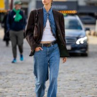 Guest wears denim jeans, shirt, brown oversized blazer outside Ganni during the Copenhagen Fashion Week Spring/Summer 2024 on August 10, 2023 in...