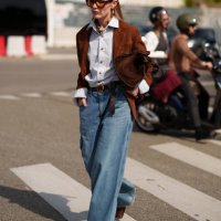 Guest wears denim wide leg jeans, a brown jacket, a bag, a blue button shirt is seen outside Prada show during the Milan Fashion Week Menswear...