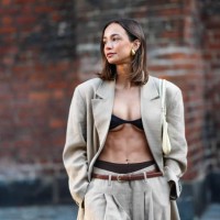 Guest wears earrings, a gray / beige full look, black bras and underwear, an opened oversized blazer jacket, a brown leather thin belt, flared pants...