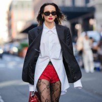 Guest wears earrings, sunglasses, a white shirt, a black oversized blazer jacket, red sequined mini shorts, black mesh tights with floral embroidery,...