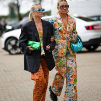 Guest wears flashy blue sunglasses, silver large earrings, a gold small necklace, a black oversized blazer jacket, a green shiny leather clutch, a...