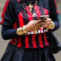 Guest wears football jersey, red and black vertical stripes, layered long-sleeve top, gold statement bracelets, stacked rings, gold cross necklace,...