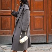 Guest wears gold earrings, a black and blue print pattern V-neck short dress, a gray oversized long coat, a white latte leather handbag, beige shiny...