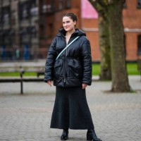 Guest wears gold earrings, gold long pendant earrings, a black shiny leather hoodie / belted coat, a pale blue shiny leather crossbody bag, a black...
