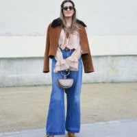 Guest wears gold hoop earrings, dark brown sunglasses, dark brown suede unzipped jacket, light pink long sleeve shirt, navy blue flared denim jean...