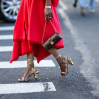 Guest wears gold large earrings, a red polar oversized puffy sleeves / belted coat, a red matching polar asymmetric midi skirt, a gold large ring, a...