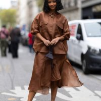 Guest wears gold pumps embellished with rhinestones, a brown leather mini bag, a gold necklace and a brown coord set outside Akris show during...