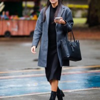 Guest wears gray overcoat, black dress, black high-heeled boots, black leather tote bag, sunglasses at Sao Paulo Fashion Week 2024 N58 - Street Style...