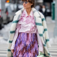 Guest wears green white checkered coat, pink blouse with appliquéd flowers, fringed pink purple skirt outside Michael Kors during New York Fashion...