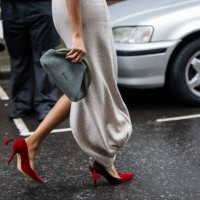 Guest wears grey green blue clutch, red heels, grey dress outside JW Anderson during London Fashion Week February 2024 on February 18, 2024 in...