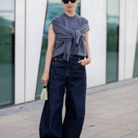 Guest wears grey sleeveless knit, dark denim jeans outside Munthe during day four of the Copenhagen Fashion Week SS25 on August 08, 2024 in...