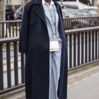 Guest wears light blue decorated vest, light blue suit, blue coat, white Chanel bag, outside Chanel, during the Womenswear Fall/Winter 2024/2025 as...