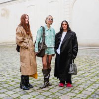 Guest wears light brown belted trench coat, shiny black belted laced boots leather shoes. Violet Grace Atkinson wears light blue sunglasses, silver...