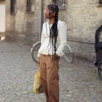 Guest wears light cream white shirt and brown pants, yellow bag and pearls as hair accessories outside the Herskind show during day three of the...
