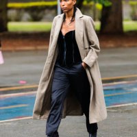 Guest wears long beige coat, black corset top, black pants, black ankle boots, braided hairstyle at Sao Paulo Fashion Week 2024 N58 - Street Style at...