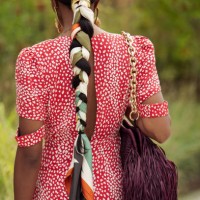 Guest wears long red dress with polkadots, burgundy bag with tassels, golden earrings and braid braided with scarf outside the Marimekko show during...