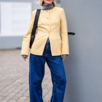 Guest wears Miu Miu sunglasses, golden earrings, a pale pastel yellow jacket, a black leather bag, blue denim jeans pants , pointed shoes, outside...