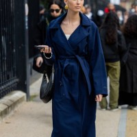 Guest wears navy belted trench coat, black bag, beige pants outside Lacoste during the Womenswear Fall/Winter 2024/2025 as part of Paris Fashion Week...