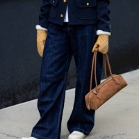 Guest wears navy jacket, jeans, Alaia bag in brown, beige gloves outside Ulla Johnson during New York Fashion Week on February 09, 2025 in New York...