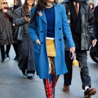 Guest wears orange sunglasses, a yellow teddy mini skirt, a blue sweater, a gold necklace, silver necklaces, a light blue teddy coat, an english flag...