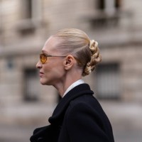 Guest wears orange sunglasses. White loose shirt, white loose over the knee skirt, black coat, outside Miu Miu, during the Paris Fashion Week...
