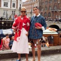 Guest wears pale pink skirt, blue ballerina shoes, red and pink pattern coat and red bag and a guest wears brown mini skirt, blue denim shirt, red...