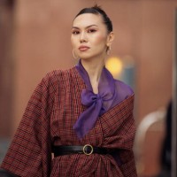 Guest wears purple tights, a brown long coat, and black long leather boots during the Tashkent Fashion Week 2023 on November 27, 2023 in Tashkent,...