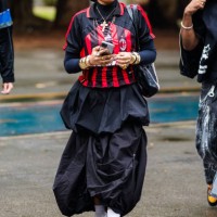 Guest wears red and black football jersey, black pleated skirt, gold jewelry, white socks, chunky sneakers at Sao Paulo Fashion Week 2024 N58 -...